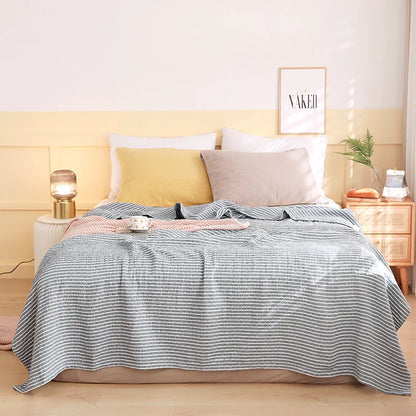 Bed with striped blanket and pillows in a bedroom setting. Boho Lightweight microfiber summer blanket for bed or sofa, cooling breathable throw for home, dorm, or office naps with geometric jacquard pattern.