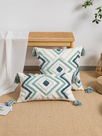 Decorative pillows with geometric patterns and tassels on a beige surface.
