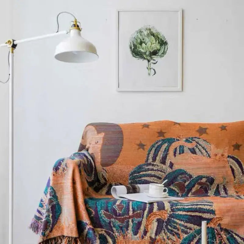 Decorative blanket with animal pattern draped over a sofa in a room with a lamp and wall art. Fringed tapestry throw blanket with black cats and pumpkins, spooky bohemian Halloween home accessory