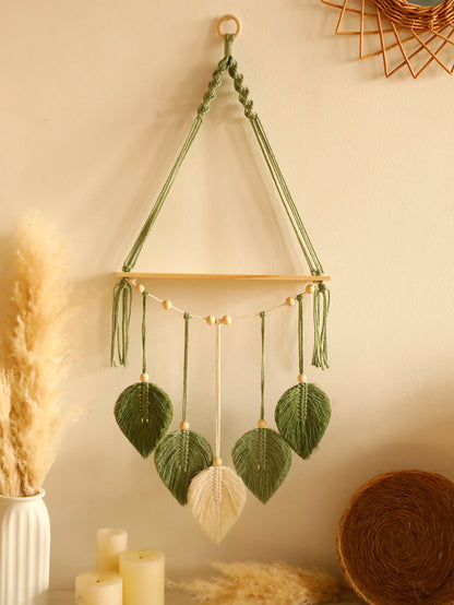 Decorative wall hanging with green leaves and a beige ball, hanging on a neutral wall.