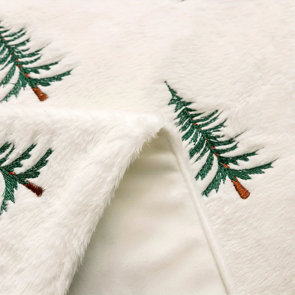 Close-up of a white fabric with embroidered green trees and red berries.