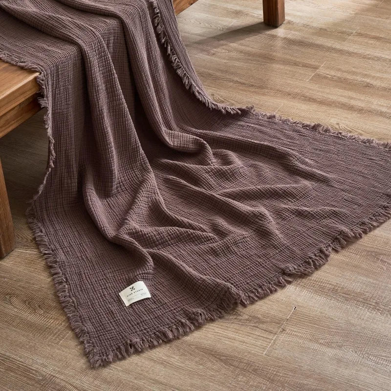 Brown textured blanket with frayed edges on a wooden floor Maillard cotton gauze blanket with tassels, four-layer muslin throw for sofa, bed, and boho home decor