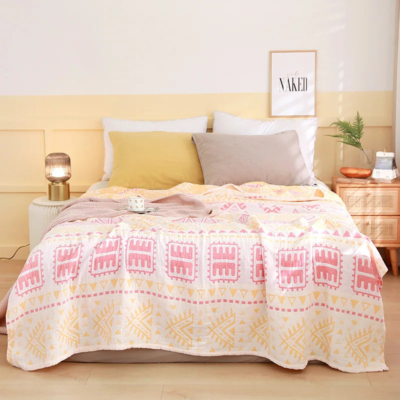 Bed with a patterned pink and yellow blanket, white pillows, and a nightstand with a lamp. Boho Lightweight microfiber summer blanket for bed or sofa, cooling breathable throw for home, dorm, or office naps with geometric jacquard pattern..