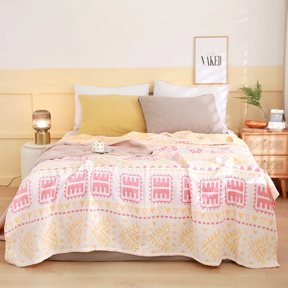 Bed with a patterned pink and yellow blanket, white pillows, and a nightstand with a lamp. Boho Lightweight microfiber summer blanket for bed or sofa, cooling breathable throw for home, dorm, or office naps with geometric jacquard pattern..