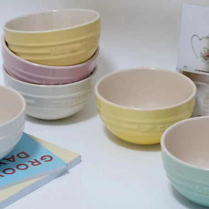Stacked ceramic bowls in pastel colors on a white surface with a magazine underneath. Gradient ceramic rice bowl in bright colors, bone china soup and noodle bowl, dessert and pudding kitchen tableware for boho home dining