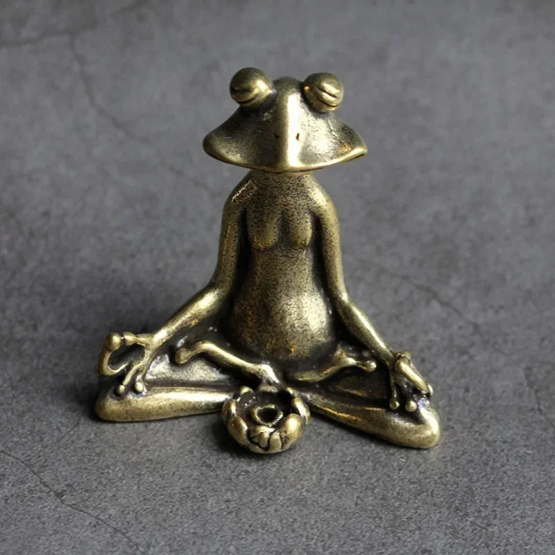 Bronze frog figurine in a meditative pose on a gray background