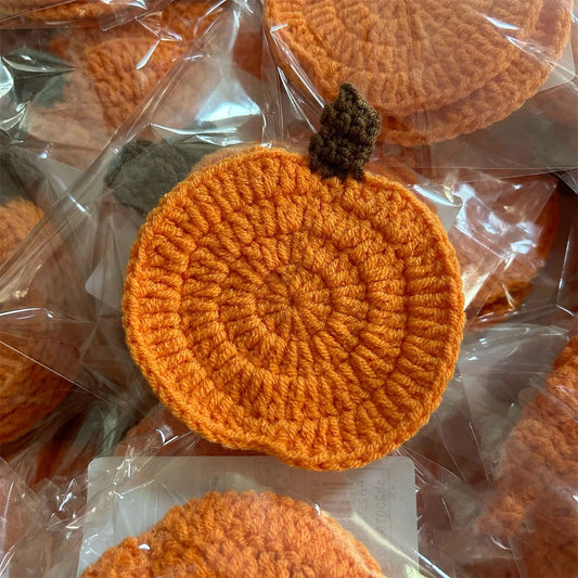 Crocheted orange pumpkin coasters on a clear plastic background. Handmade crochet pumpkin coaster in cotton, Halloween table decor for mugs and drinks, festive DIY autumn party accessory