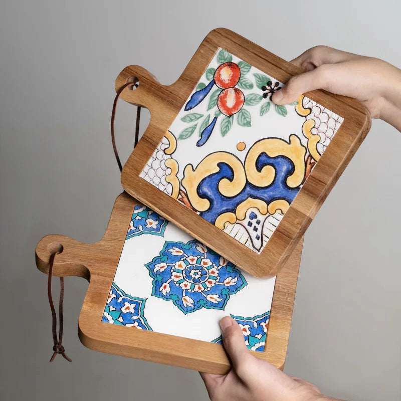 Decorative tray with floral patterns and wooden frame held by hands against a gray background
