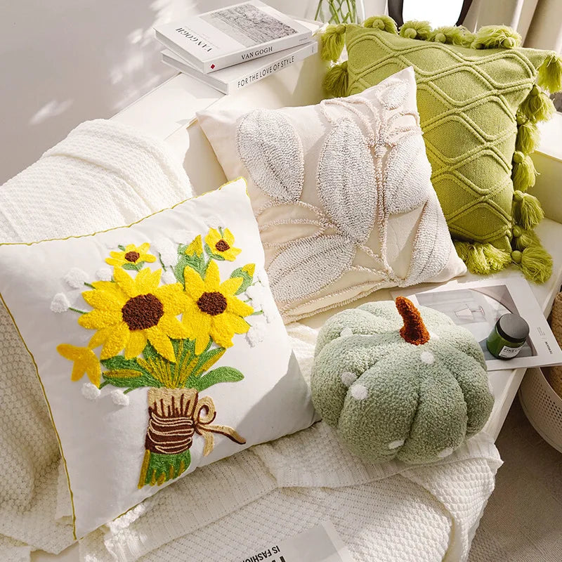 Decorative pillows with floral design, leaf pattern, and green pumpkin on a white surface.