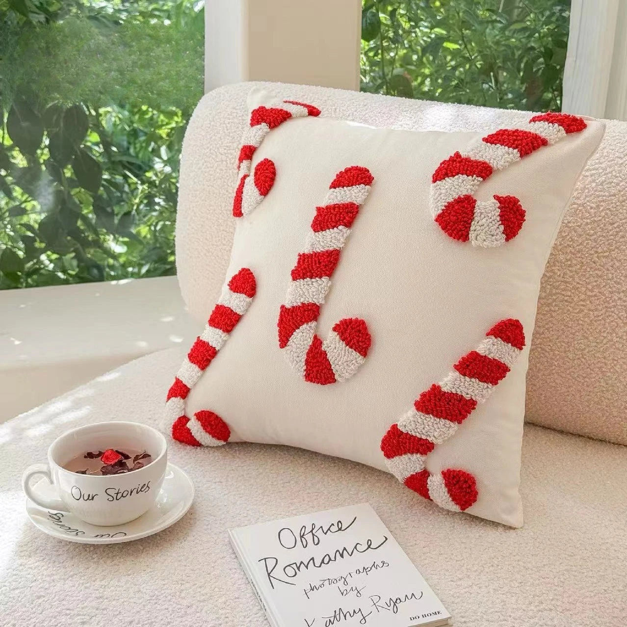 Decorative pillow with candy cane design on a couch with a cup and book.