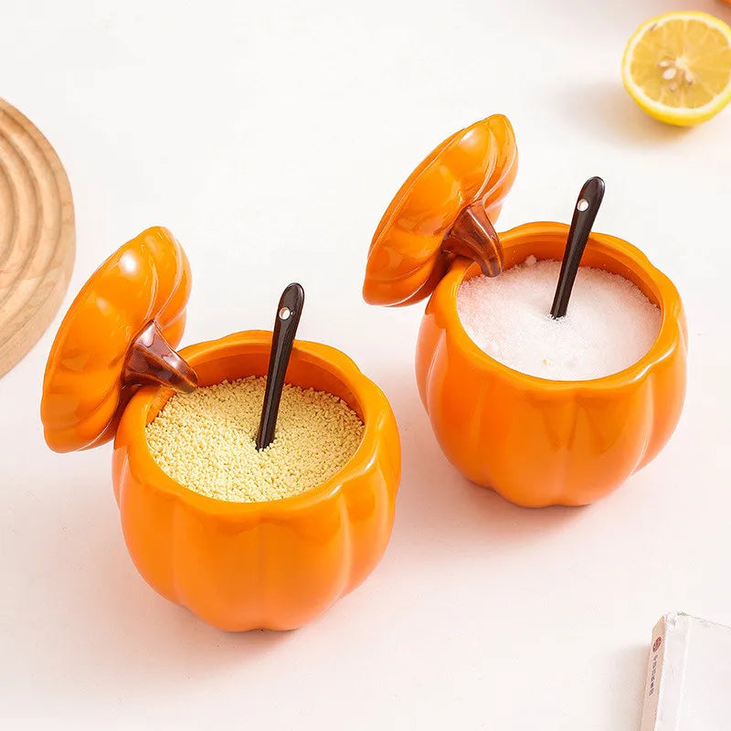 Two orange pumpkin-shaped salt and pepper shakers with spoons on a light background. Pumpkin-shaped ceramic bowl with lid kitchen container Halloween and Thanksgiving fall serving dish