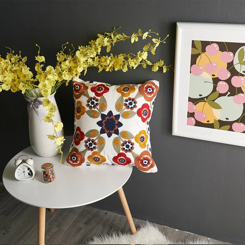 Decorative pillow with floral pattern on a small round table against a dark wall with a framed picture. floral embroidery on linen cotton cushion cover – boho home decor accent