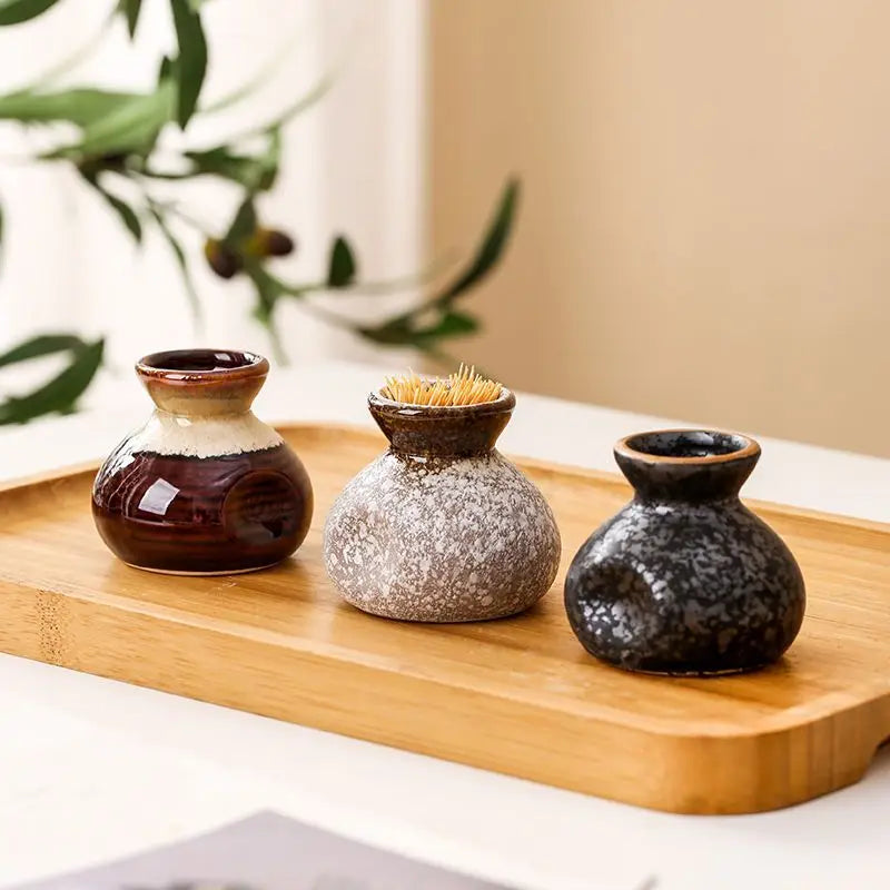 Three small decorative vases on a wooden tray with a blurred plant in the background.