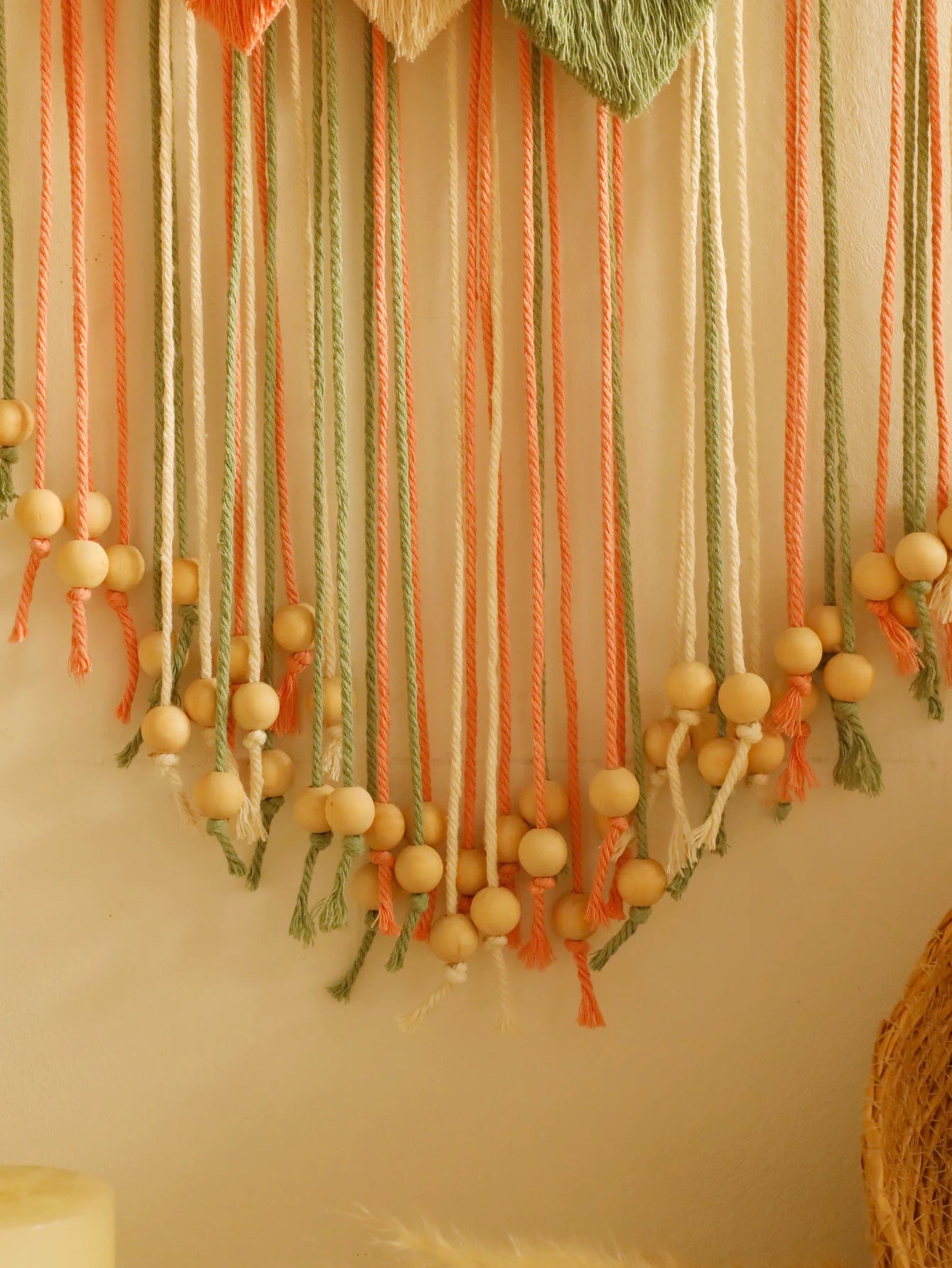 Decorative wall hanging with yarn strands and wooden beads on a neutral background
