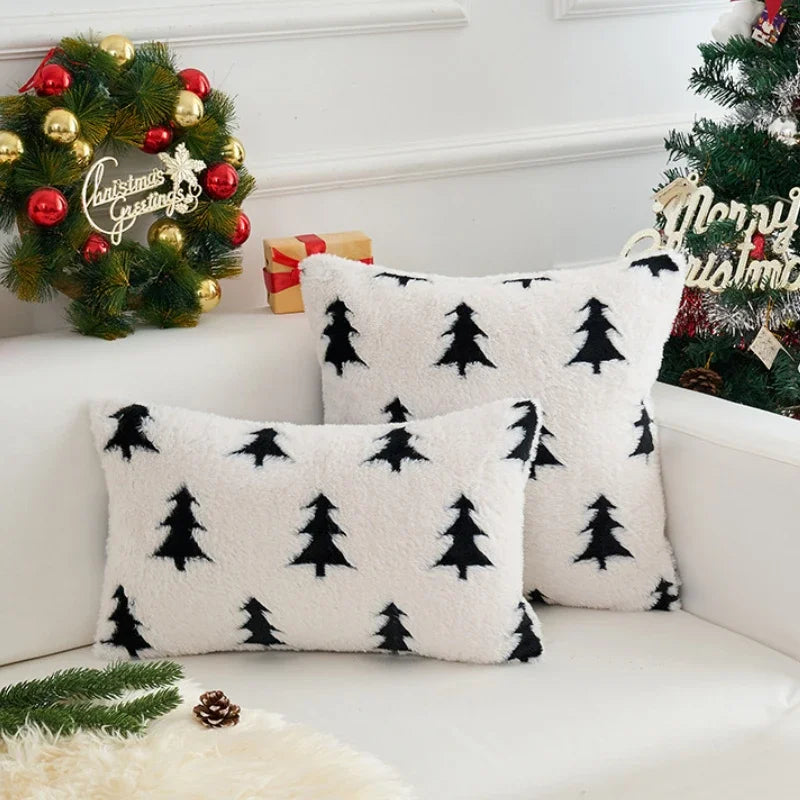 White pillows with black tree patterns on a white couch with Christmas decorations.