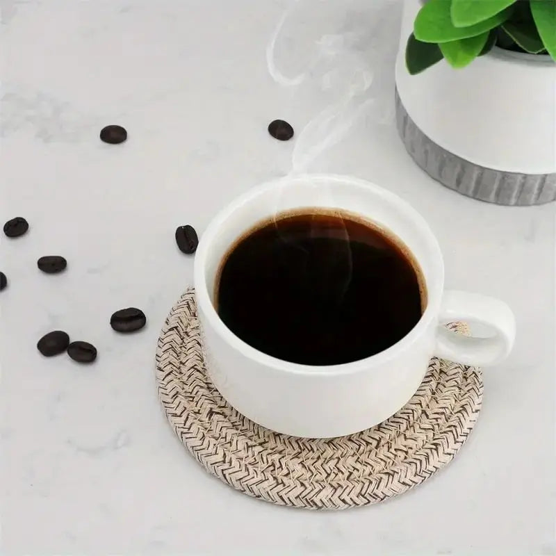 White mug of black coffee on a woven coaster with scattered coffee beans and a plant in the background. Set of cotton drink coasters – eco-friendly housewarming gift idea