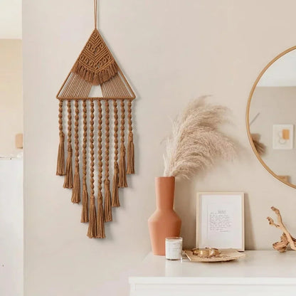 Macrame wall hanging on a neutral wall with decorative items below. boho home decor, macrame wall hanging, triangle dream catcher, woven tapestry, handmade cotton wall decor, tassel wall hanging, bedroom door decor, housewarming gift, rustic bohemian art, boho apartment wall decor, neutral textile art
