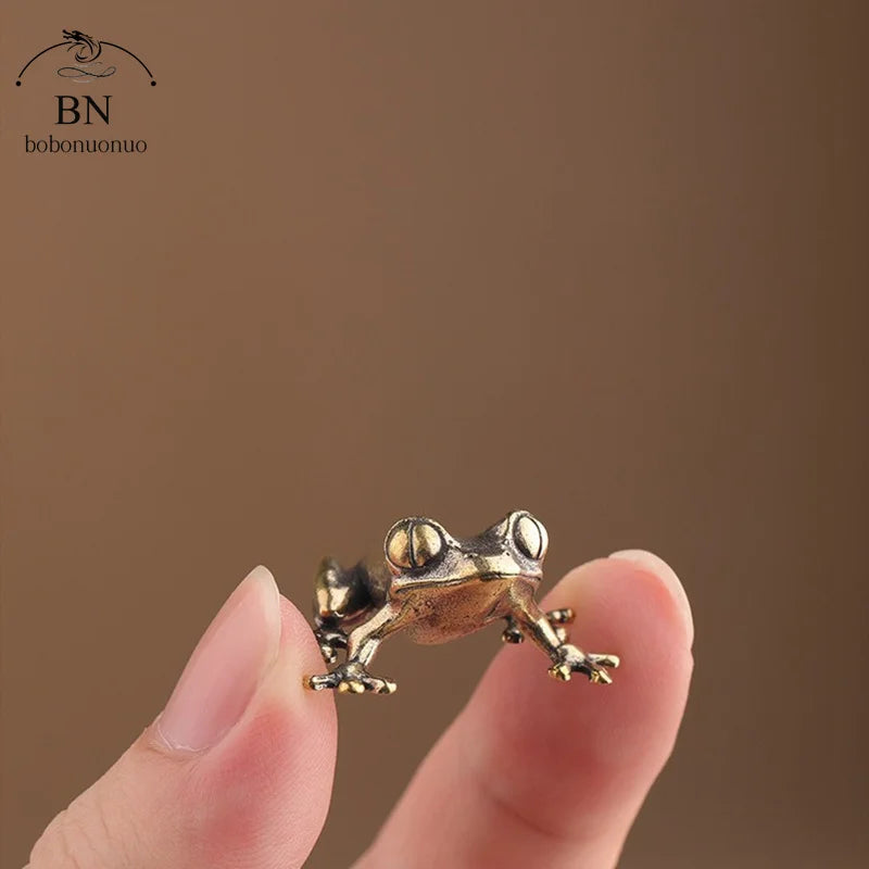 Small bronze frog figurine held between fingers against a brown background