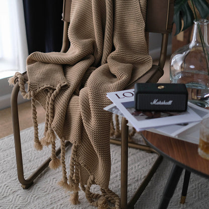 Brown knitted blanket draped over a chair with a Marshall speaker and magazine on a table in the background.