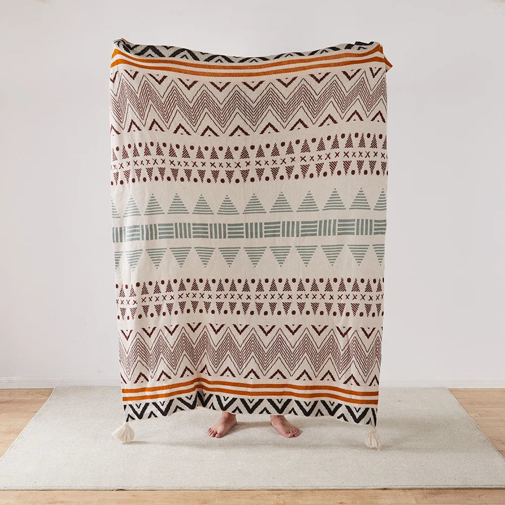 Patterned Bohemian blanket draped over a person on a light wooden floor with a white wall background