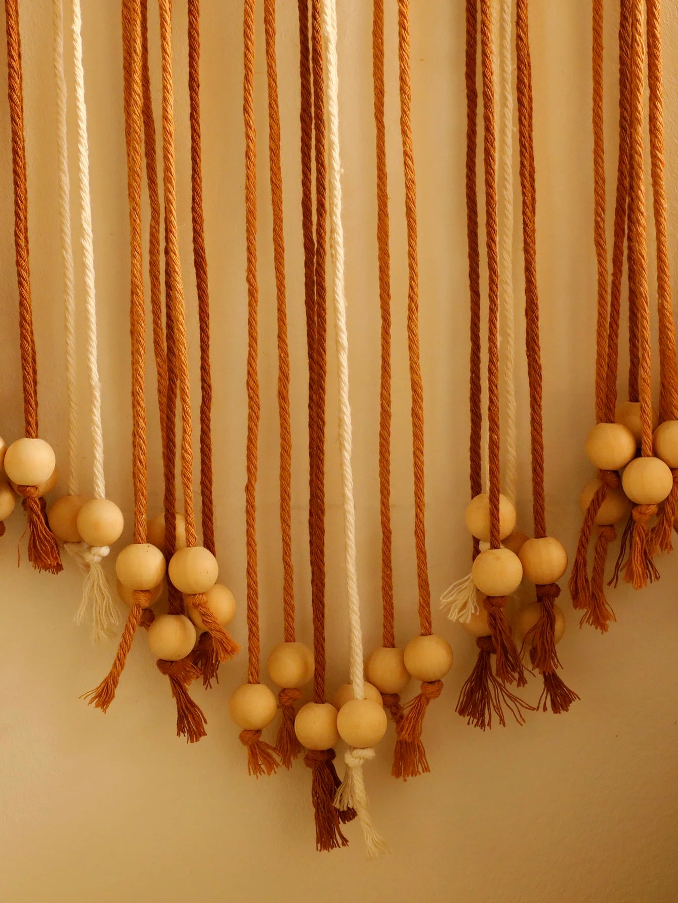 Decorative wall hanging with ropes and wooden beads on a plain background