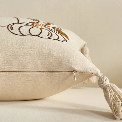 Beige pillow with embroidered design and tassel on a beige background. Festive autumn pumpkin cushion case for sofa or bed