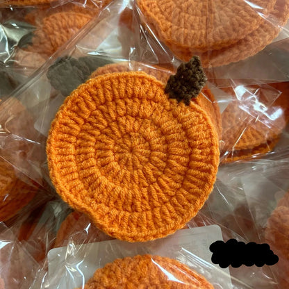 Orange crocheted items on clear plastic packaging. Handmade crochet pumpkin coaster in cotton, Halloween table decor for mugs and drinks, festive DIY autumn party accessory