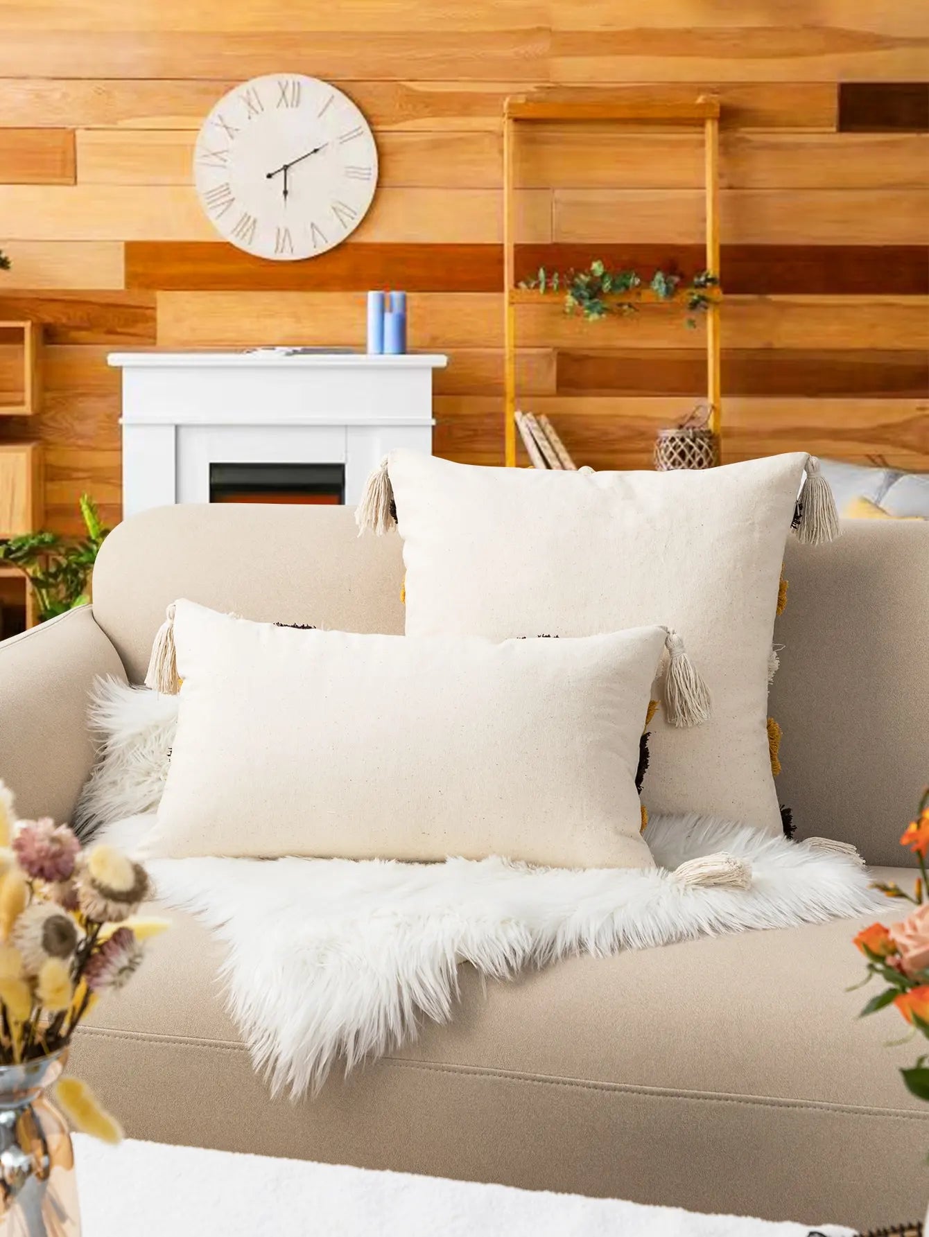 Beige sofa with white pillows in a living room setting with wooden walls and a fireplace.