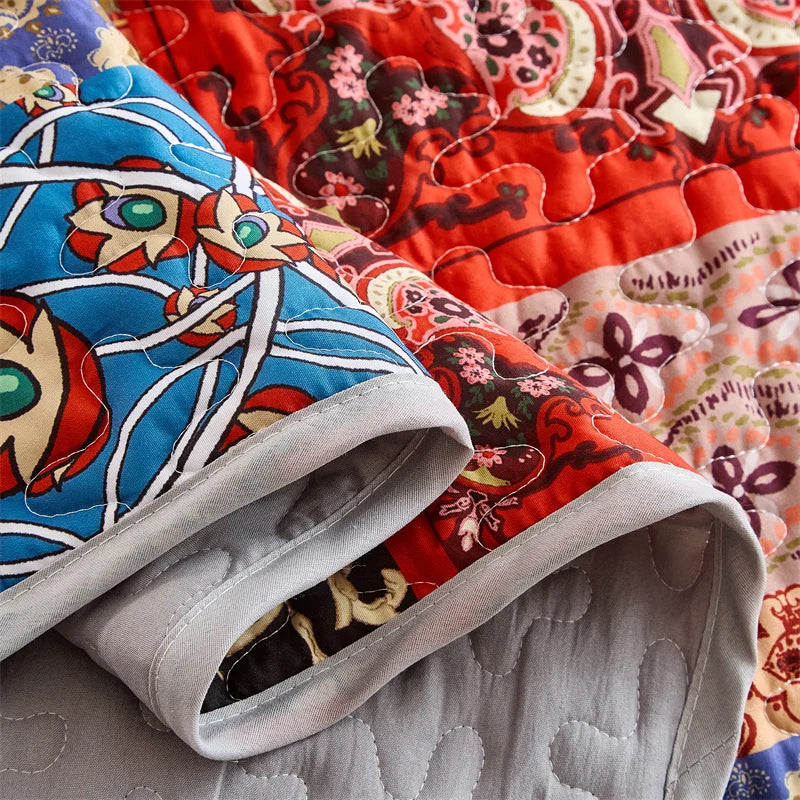 Close-up of a colorful quilt with floral patterns in red, blue, and multicolor. Lightweight boho quilted bedspread set with pillow shams, soft all-season coverlet for queen, king, full, or twin beds in modern cloud pattern design.