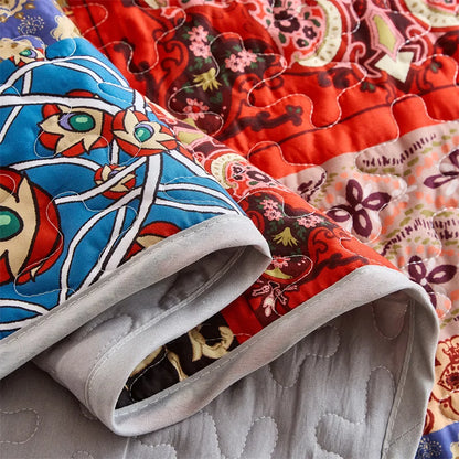 Close-up of a colorful quilt with floral patterns in red, blue, and multicolor. Lightweight boho quilted bedspread set with pillow shams, soft all-season coverlet for queen, king, full, or twin beds in modern cloud pattern design.