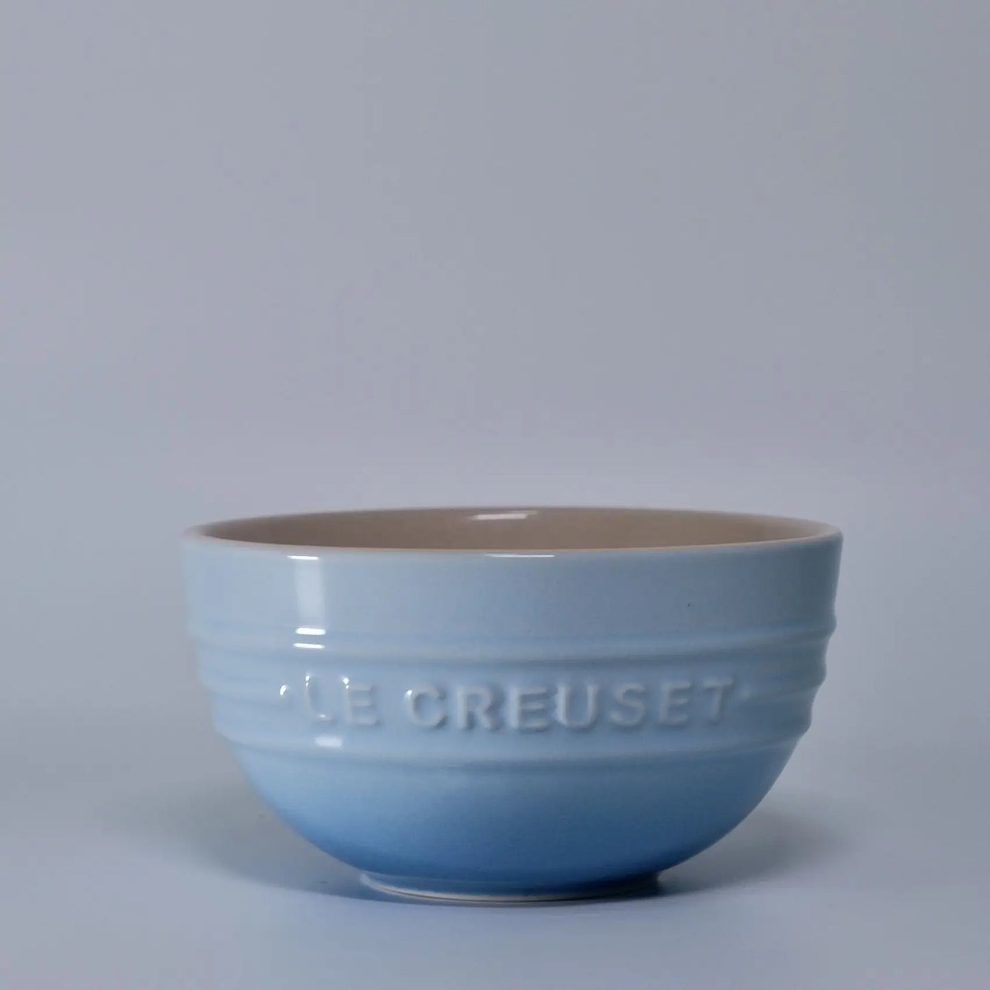 Blue ceramic bowl with 'Le Creuset' branding on a light gray background Gradient ceramic rice bowl in bright colors, bone china soup and noodle bowl, dessert and pudding kitchen tableware for boho home dining