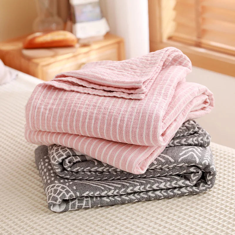 Stack of folded pink and gray blankets on a bed. Boho Lightweight microfiber summer blanket for bed or sofa, cooling breathable throw for home, dorm, or office naps with geometric jacquard pattern.