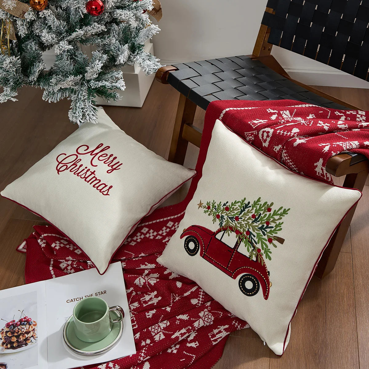 Decorative pillows with Christmas designs on a table with a red blanket and small tree. Embroidered Merry Christmas pillow cover with snowflake design – festive red and white holiday cushion for sofa or bedroom décor.