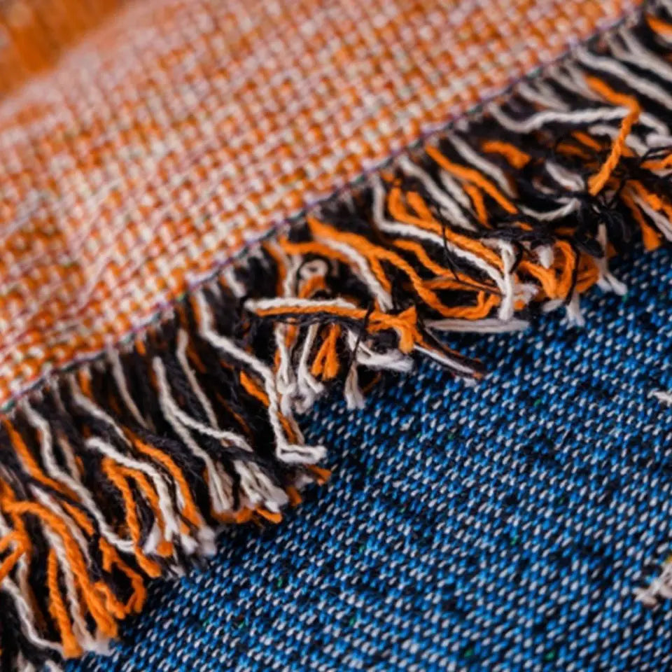 Close-up of a fabric with orange, black, and white pattern on a blue background. Cozy Halloween blanket with pumpkins and cats, boho woven couch cover for fall home decor