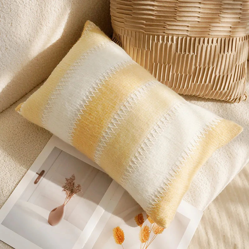 Yellow and white striped pillow on a textured surface with a woven basket in the background.
