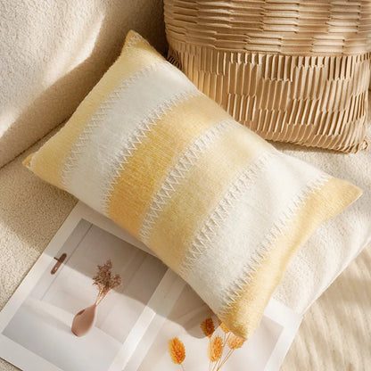 Yellow and white striped pillow on a textured surface with a woven basket in the background.