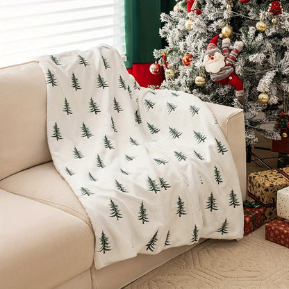 White blanket with green tree patterns draped over a beige couch in a festive living room.
