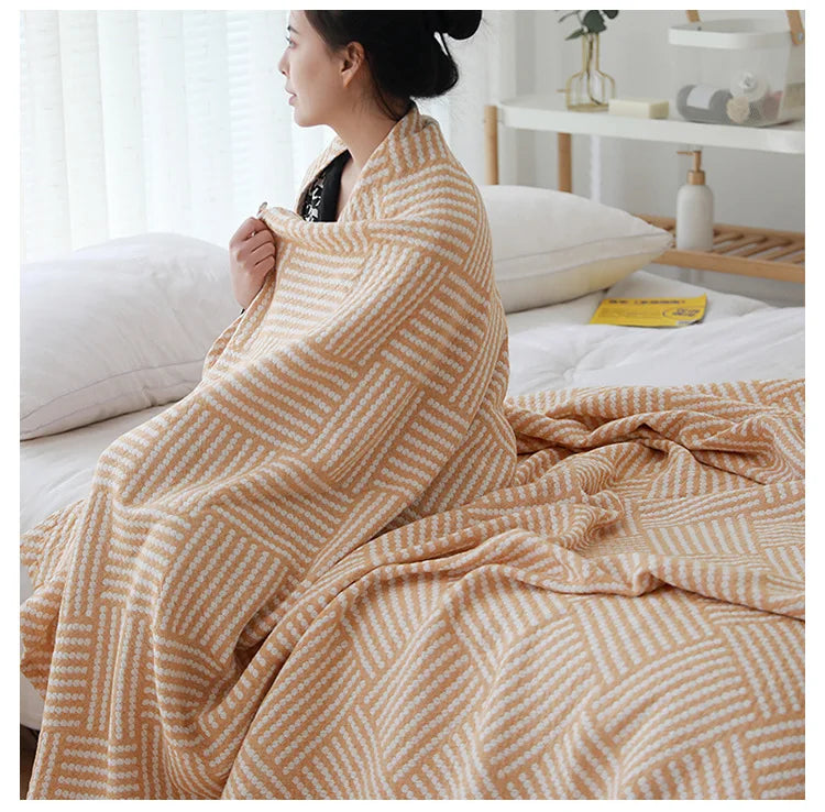 Woman wrapped in a patterned blanket on a bed in a bright room. Boho Lightweight microfiber summer blanket for bed or sofa, cooling breathable throw for home, dorm, or office naps with geometric jacquard pattern.