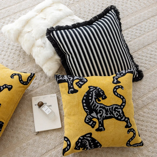 Yellow and black tiger-patterned pillows on a textured surface with a white fluffy pillow and a book. Modern minimalist embroidered pillow cover for living room decor.