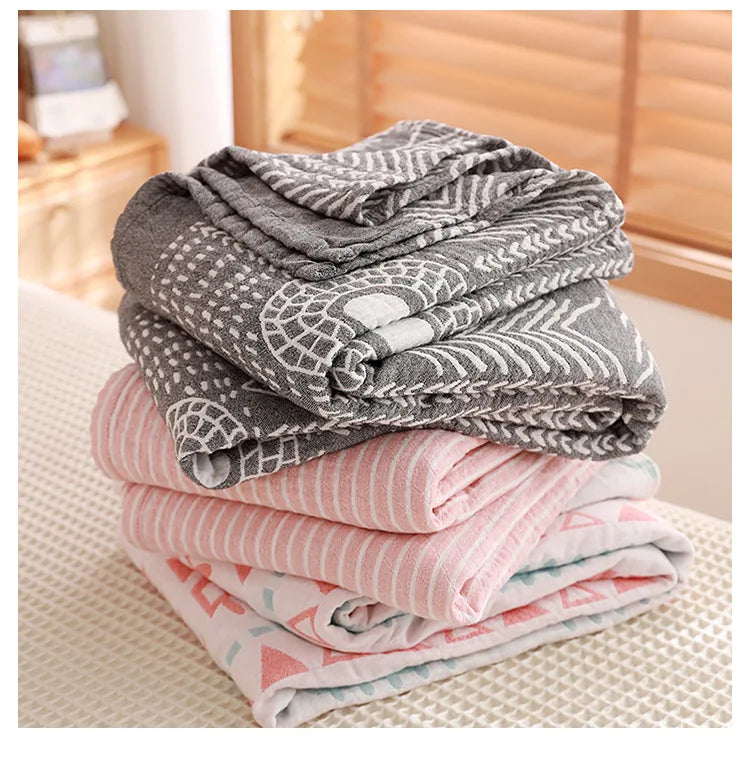 Stack of folded blankets with geometric patterns on a bed. Boho Lightweight microfiber summer blanket for bed or sofa, cooling breathable throw for home, dorm, or office naps with geometric jacquard pattern.