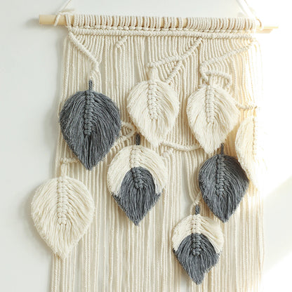 Macrame wall hanging with leaf-shaped decorations in gray and white on a light background