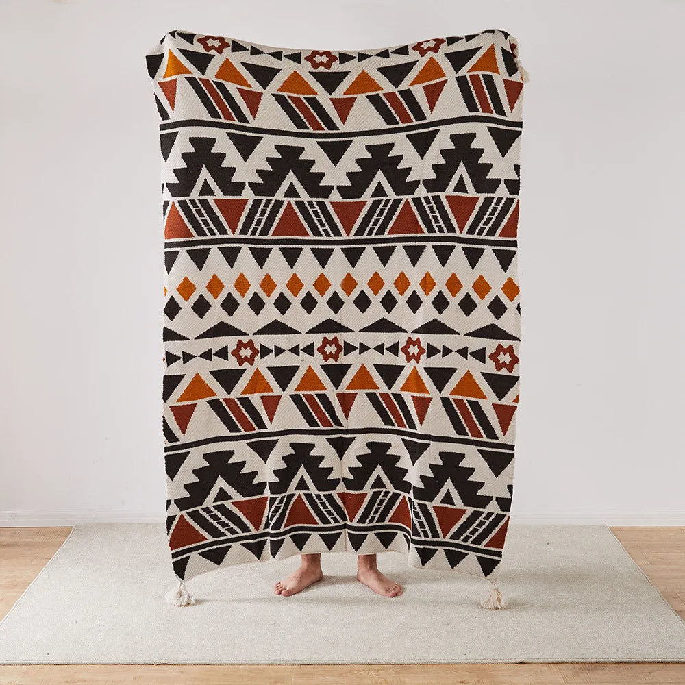 Geometric Bohemian patterned blanket draped over a person on a light wooden floor.