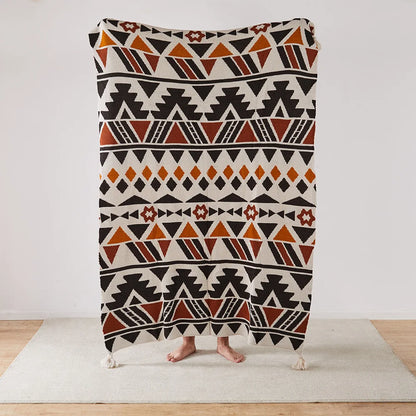 Geometric Bohemian patterned blanket draped over a person on a light wooden floor.