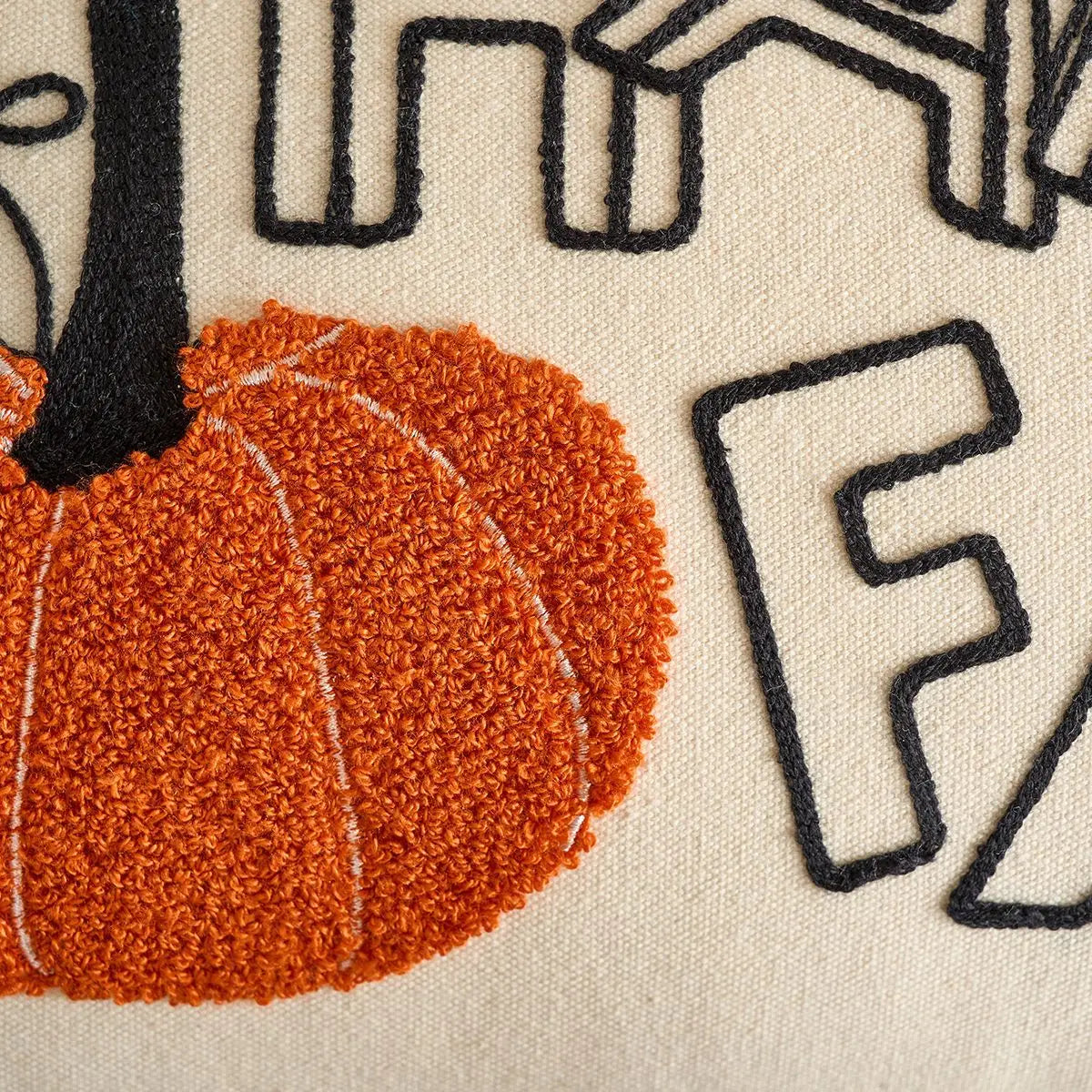 Close-up of a textured fabric with a pumpkin and black letter 'F' on a beige background. Festive autumn pumpkin cushion case for sofa or bed