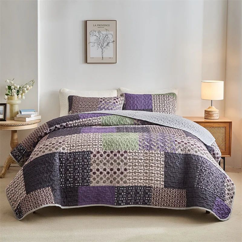 Patchwork quilt on a bed in a bedroom with a lamp and decor. Lightweight boho quilted bedspread set with pillow shams, soft all-season coverlet for queen, king, full, or twin beds in modern cloud pattern design.
