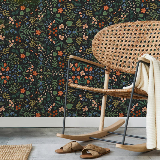 Rattan chair with a floral-patterned wall in the background. Black floral peel-and-stick wallpaper roll, 40 x 120 cm, waterproof and moisture-proof wall covering for stylish home decoration