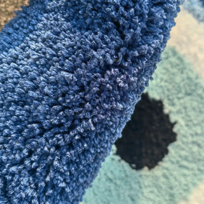 Close-up of a blue textured rug corner on a green rug. boho home decor, evil eye rug, tufted bathroom rug, fluffy circle rug, plush floor mat, round bath mat, anti-slip mat, dorm decor, Halloween decor, housewarming gift, bathroom accessories, bedroom rug, living room carpet