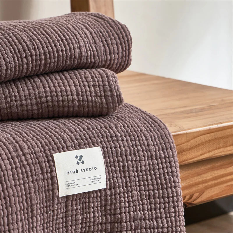 Folded brown purple textured blanket with a label on a wooden surface Maillard cotton gauze blanket with tassels, four-layer muslin throw for sofa, bed, and boho home decor