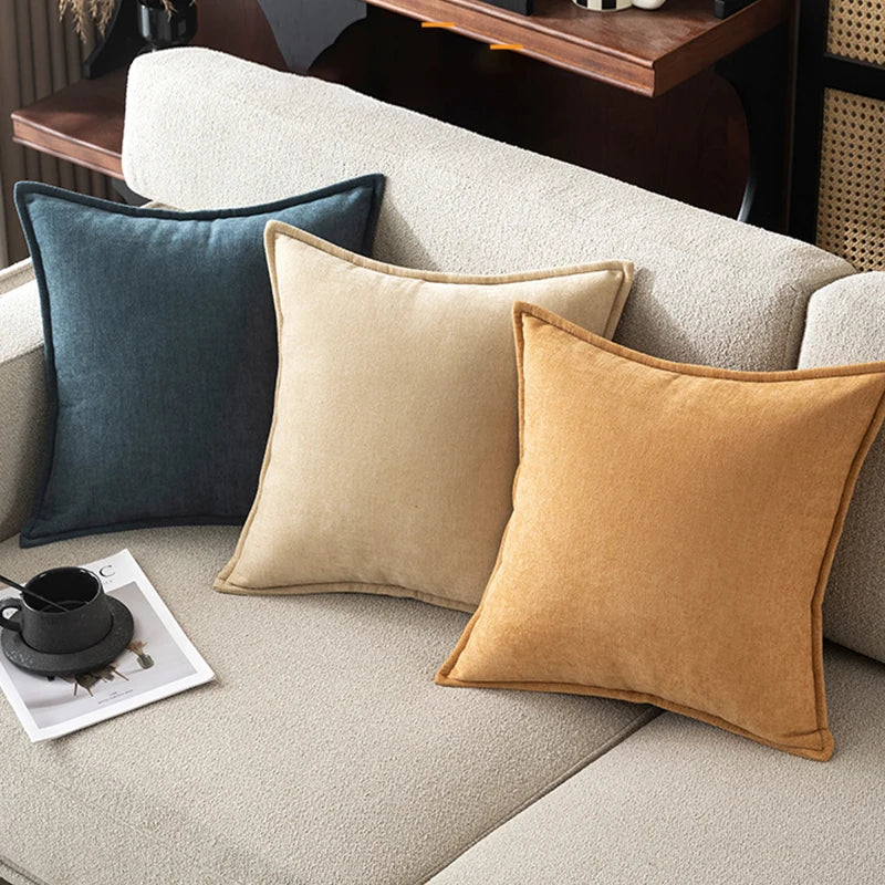 Three pillows in blue, beige, and mustard on a sofa with a magazine and cup.