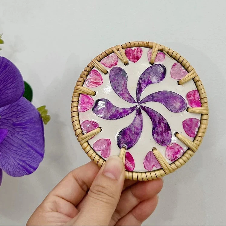 Hand holding a circular boho coaster item with a floral pattern on a plain background
